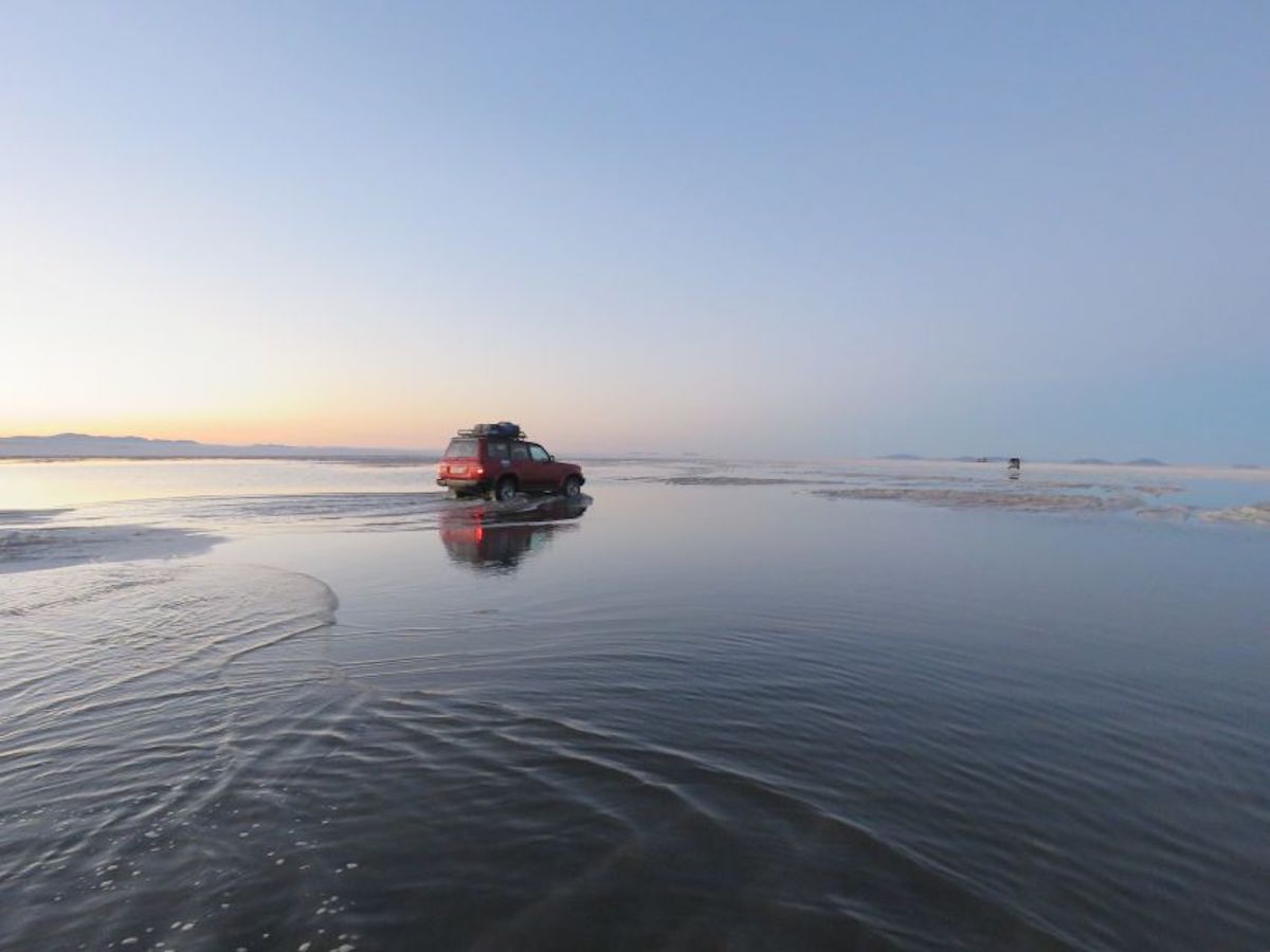 car driving over watery salar de uyuni salt flats at sunset